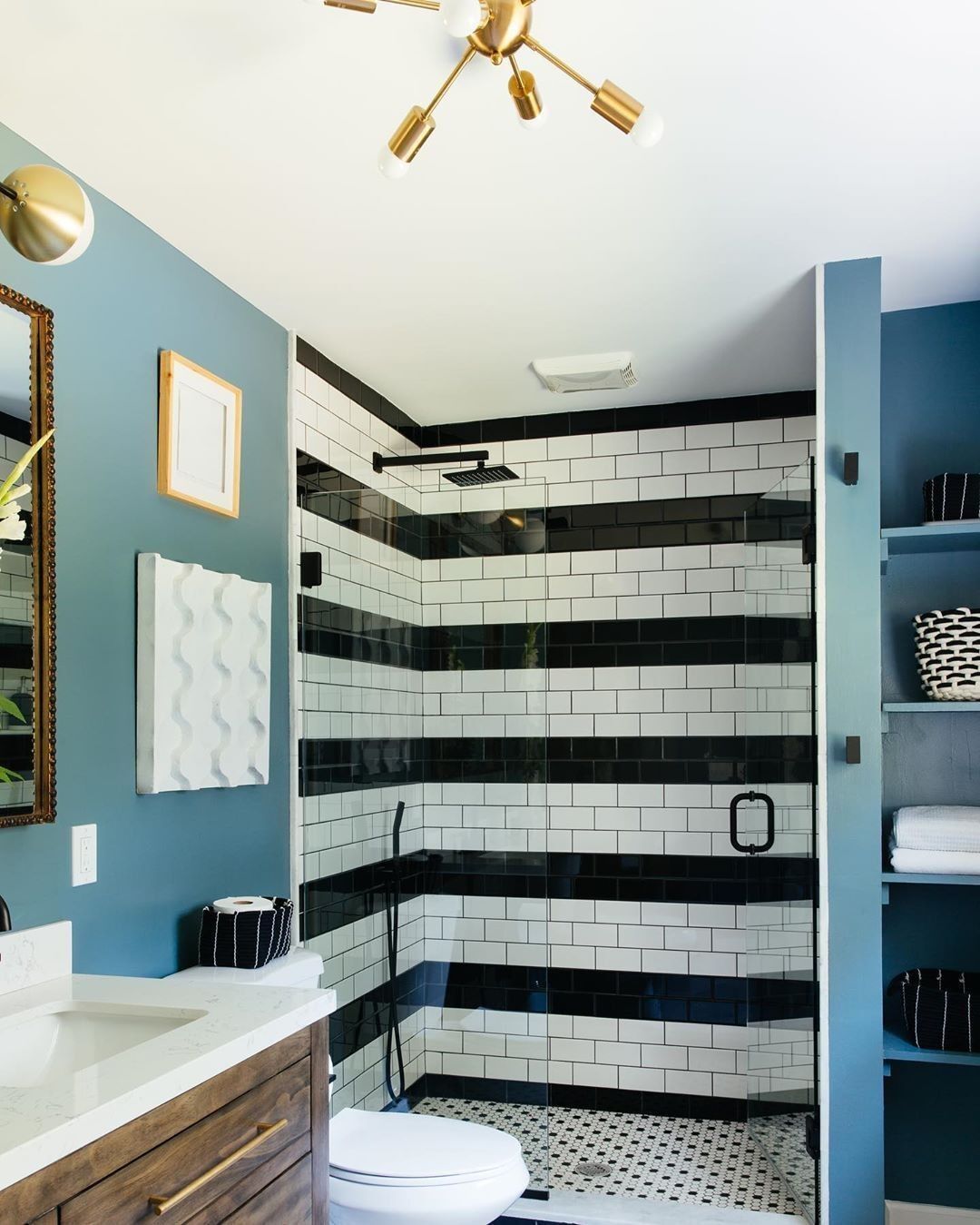 Banheiro com paredes azuis. Na parte do chuveiro, tem azulejos pretos e brancos