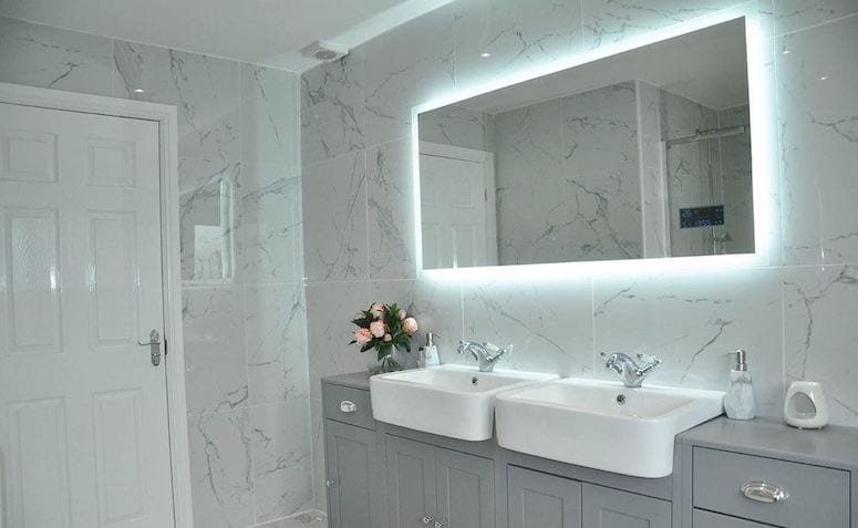 Banheiro com parede marmorizada branca. Luz branca atrás do espelho