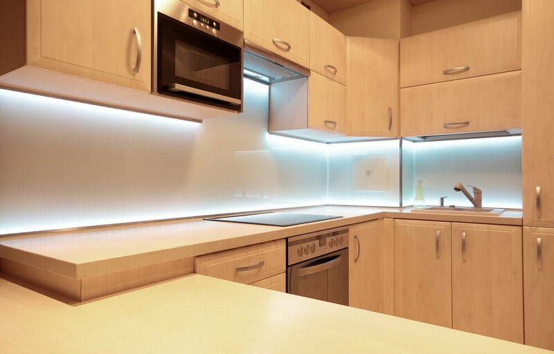 Cozinha clara com armário grande. Nas bordas desse armário, luz branca em fita